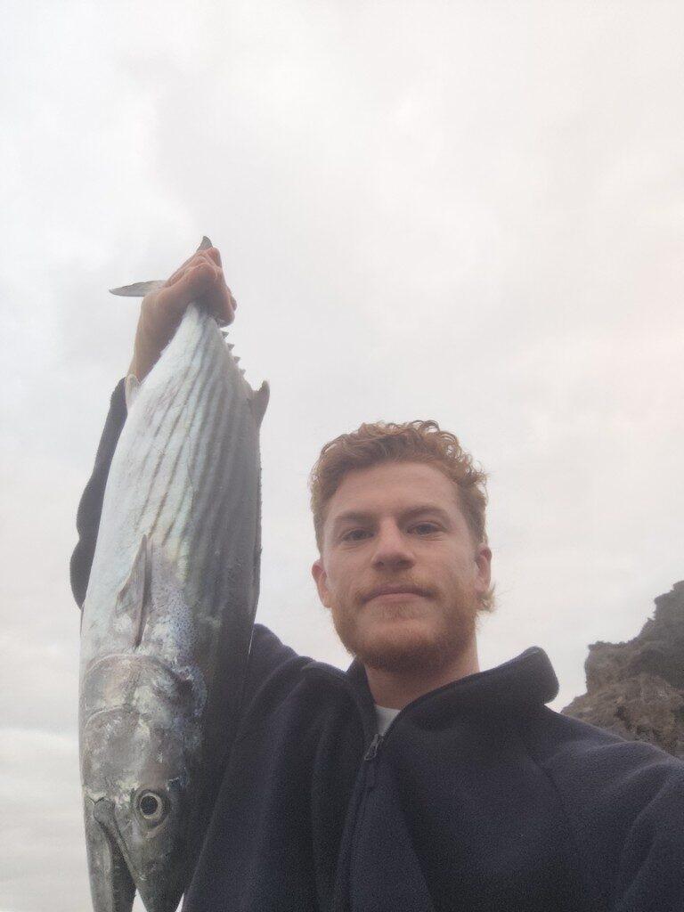 Alexis Guay holding a fish he caught, on a rocky coast